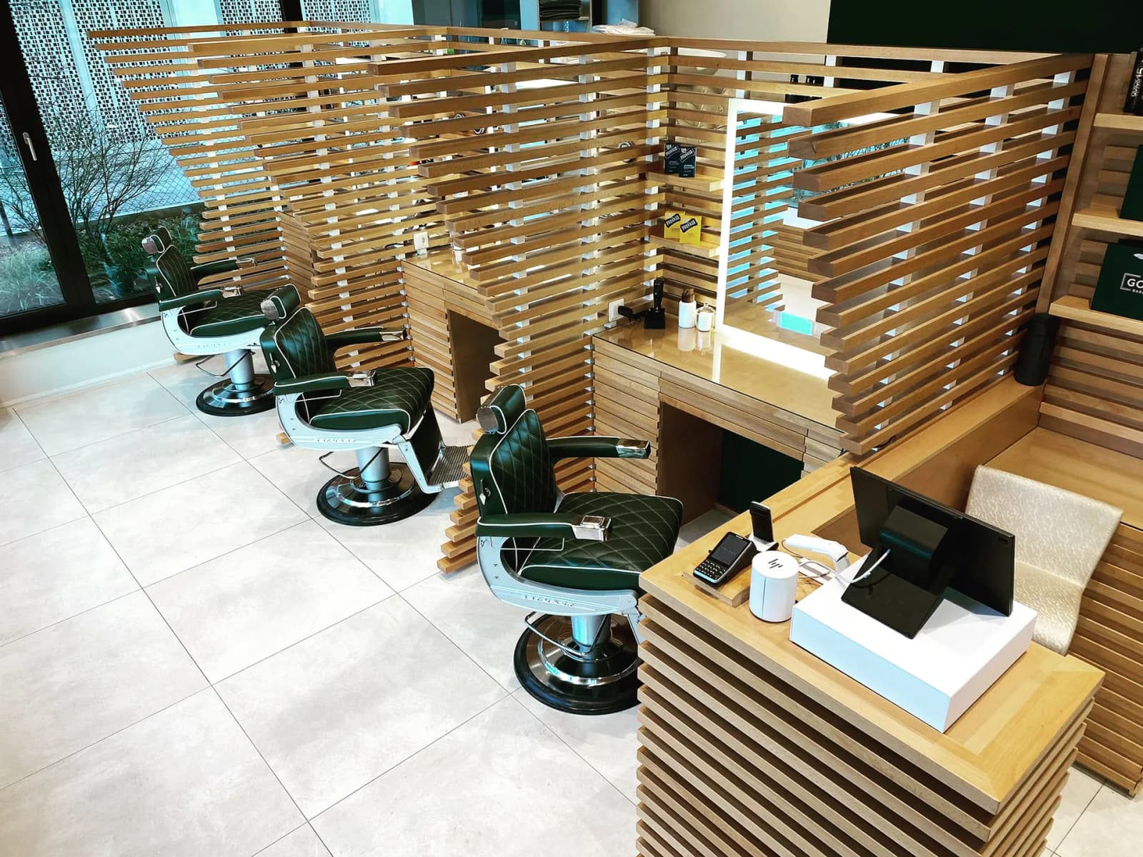Interior of The Good Barbers Enge barbershop with green leather chairs and wooden partitioned stations