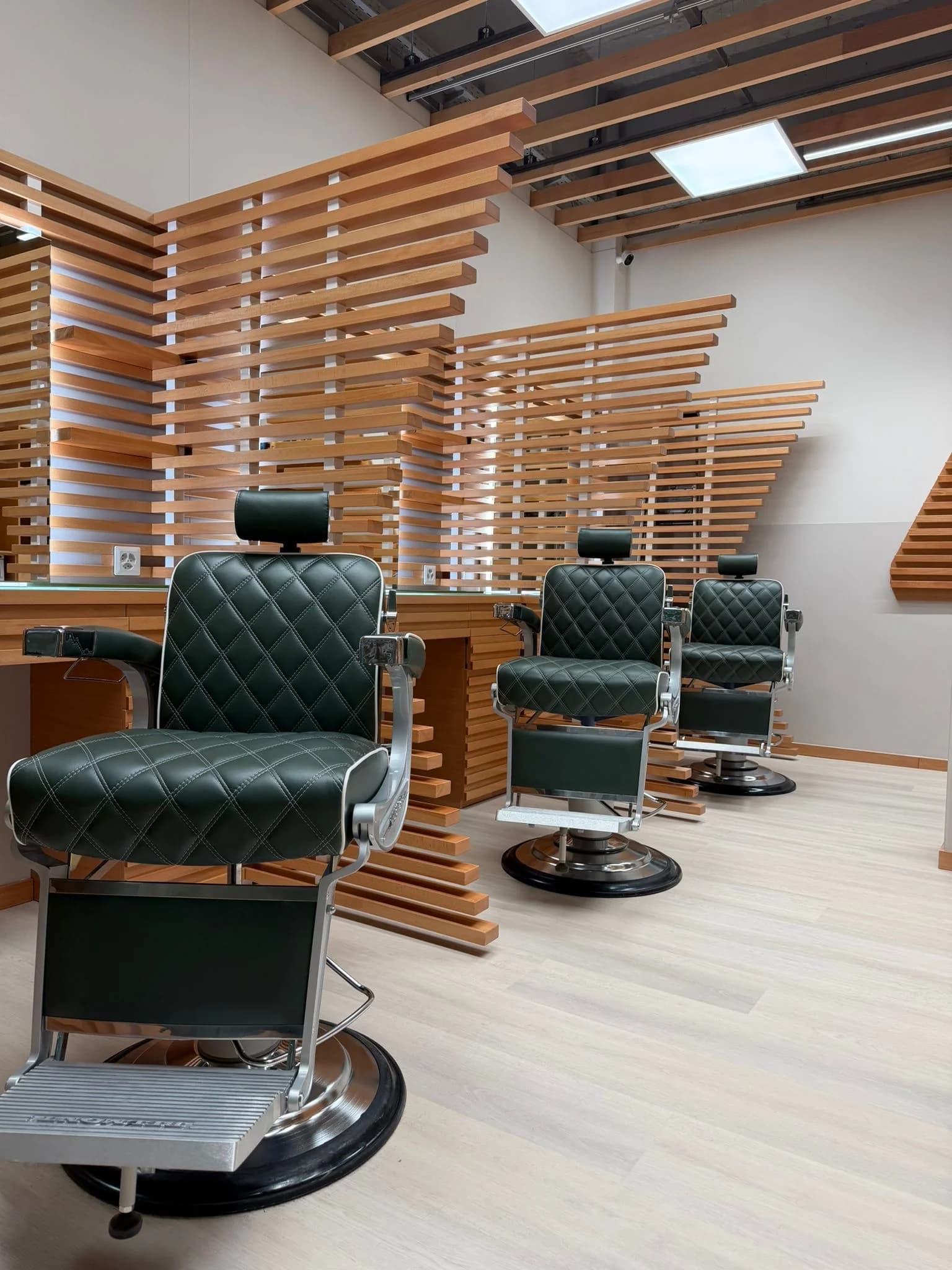 Interior of The Good Barbers Europaallee salon with wooden partitions and green barber chairs