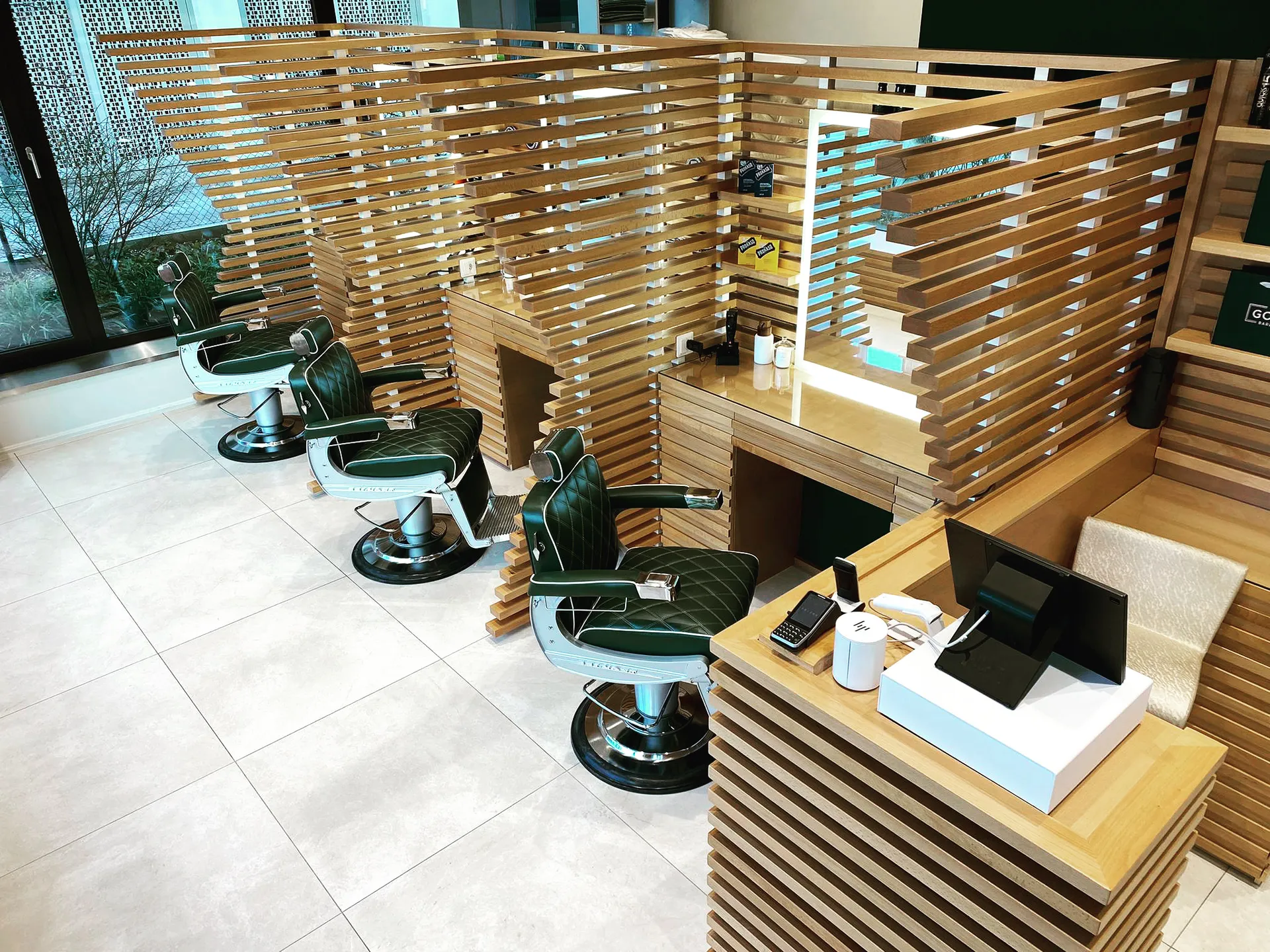 Interior of The Good Barbers Enge barbershop with green leather chairs and wooden partitioned stations